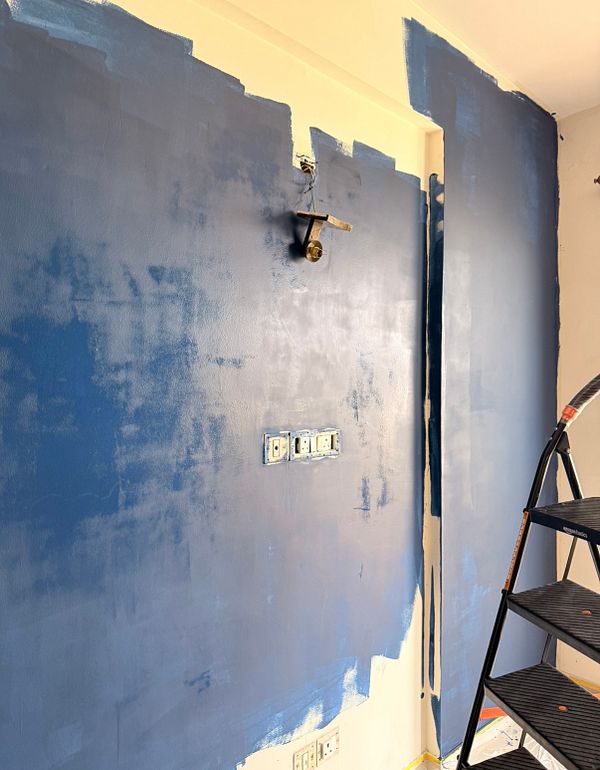 Interior wall being painted blue as part of a DIY studio renovation, with a paint step ladder in view.