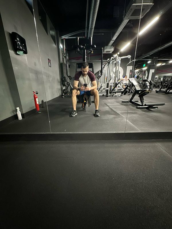 A man is seated on a bench in a gym, looking at his phone.