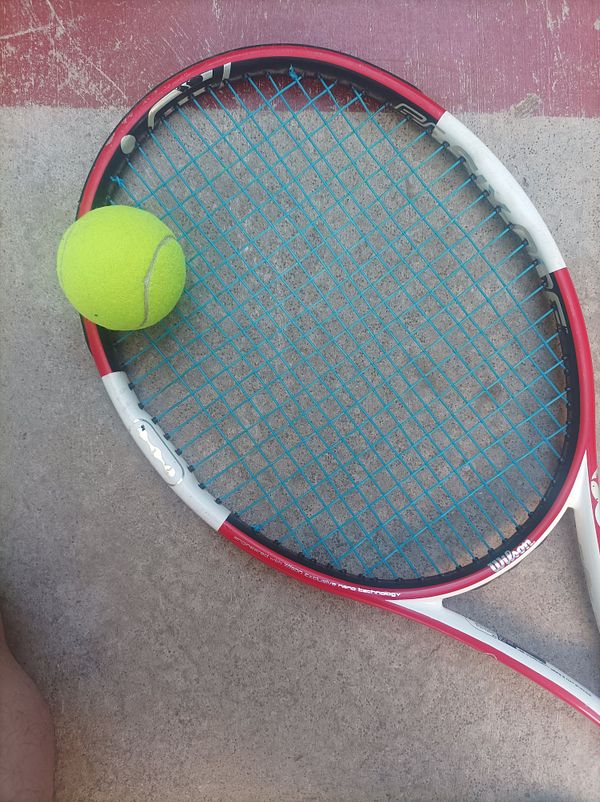 A tennis racket and a tennis ball are positioned on a concrete surface.