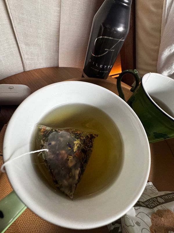 A cup of herbal tea with a tea bag steeping in it, accompanied by a water bottle and other items on a table.