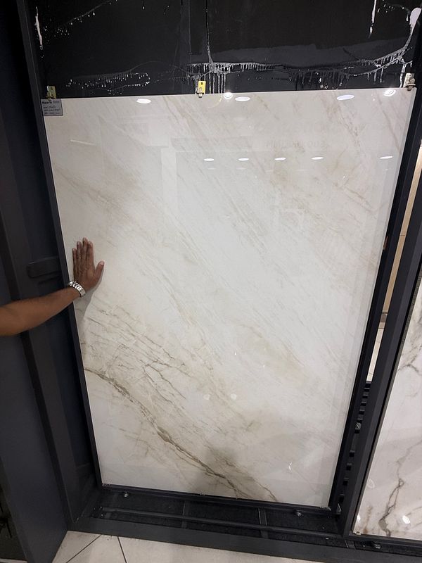 A hand is placed against a large marble-like tile in a showroom setting.