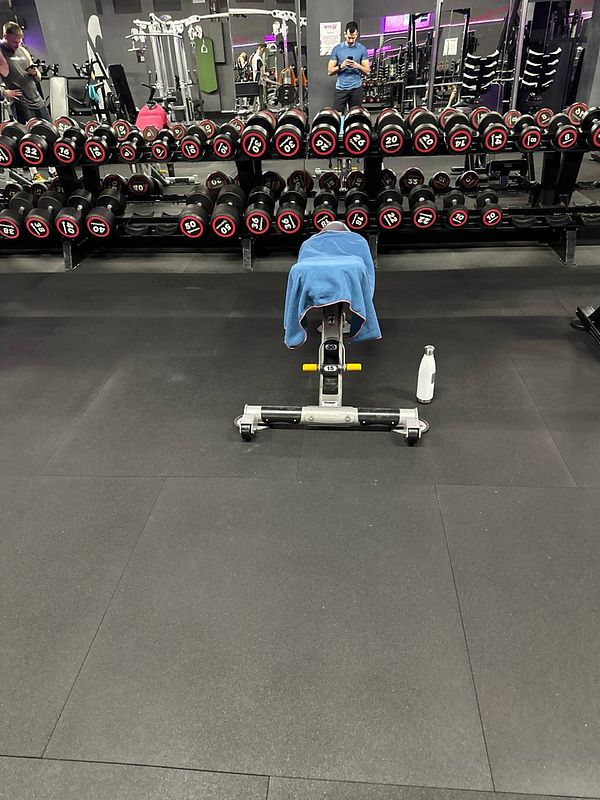 A gym scene featuring a bench, dumbbells, and a water bottle.
