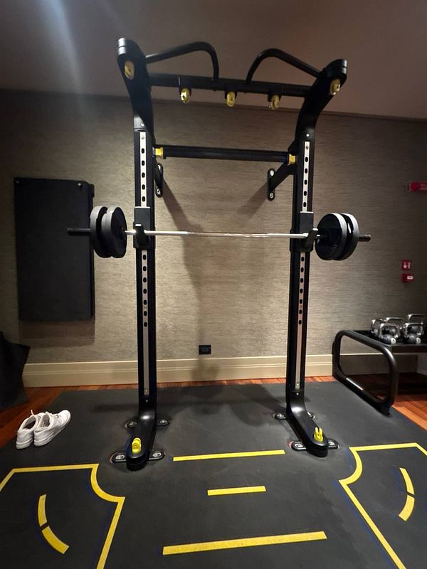 A gym setup featuring a squat rack with weights and exercise equipment in a hotel.