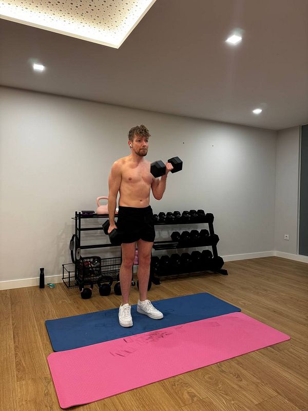 A man is performing a workout in a home gym, holding dumbbells.