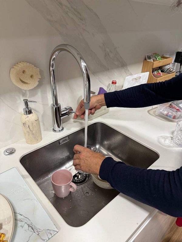 A person is filling a pink mug with water from a modern kitchen faucet.
