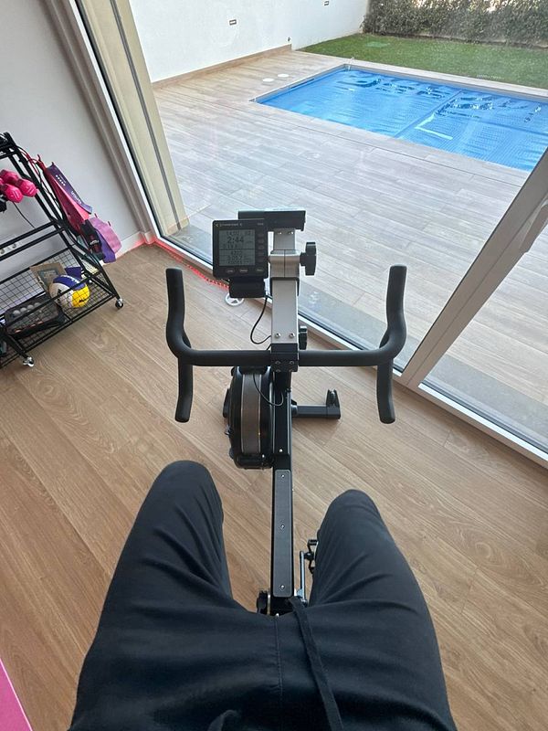 A person is seated on a rowing machine with a view of a pool outside.