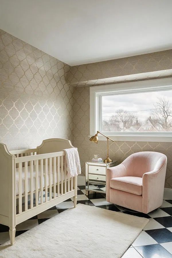A refined nursery with an ivory crib, blush pink swivel chair, mirrored nightstand, and brass desk lamp set against metallic patterned wallpaper. Black-and-white checkered tile flooring and a plush white rug add contrast and softness beneath a large window with white trim.