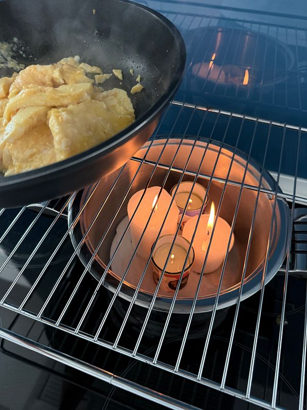 A pan of scrambled eggs is being cooked using candles as a heat source.
