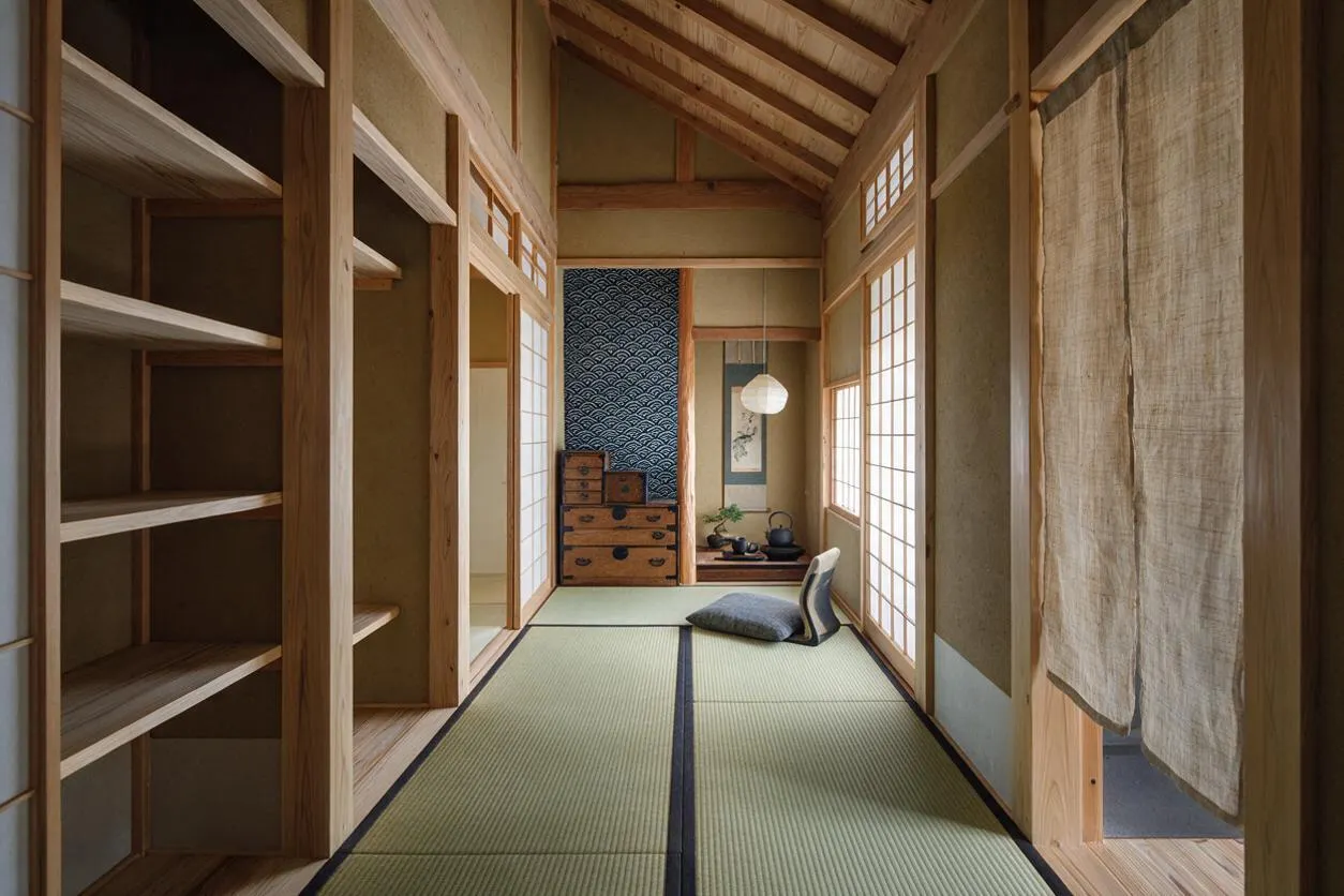 A narrow Japanese Zen-style closet or dressing room with open wooden shelving on the left, tatami mat flooring, and shoji screens lining the walls. Natural linen curtains hang on the right, and warm wood beams and trim create a calm, minimalist atmosphere.