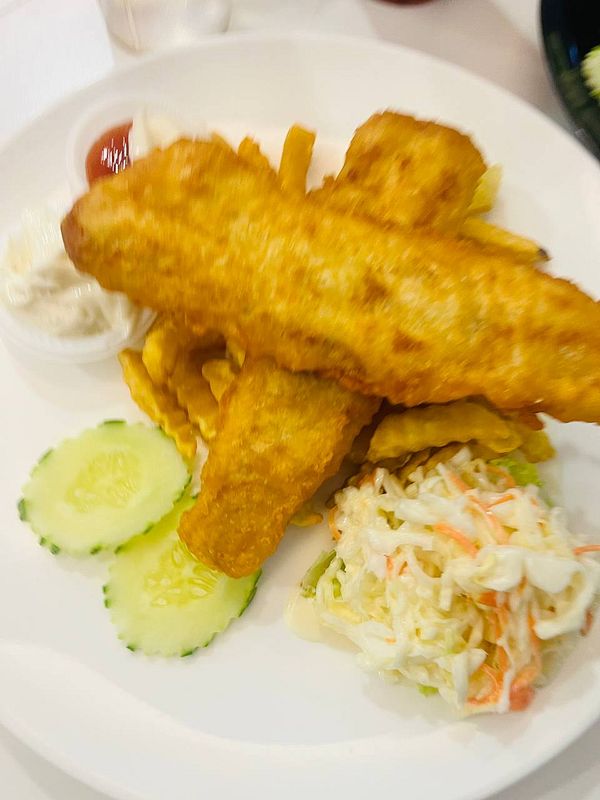 A plate of fish and chips with sides of coleslaw and cucumber slices.