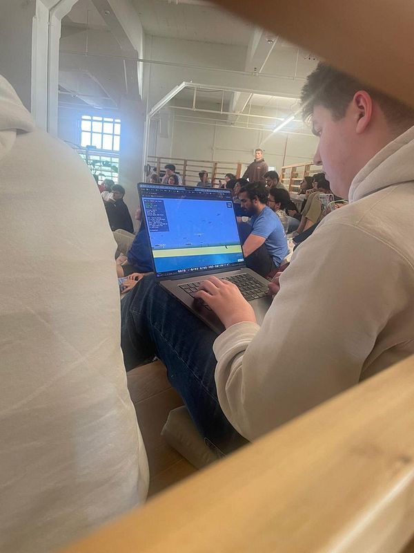 A young man is focused on his laptop while seated among a crowd at a startup event.