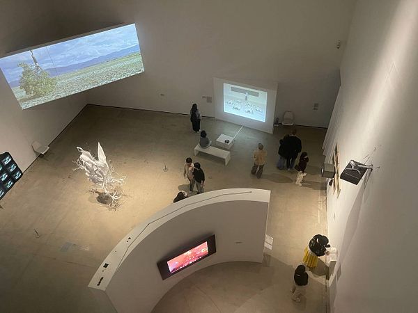 An art gallery space featuring various multimedia installations and visitors engaging with the exhibits.
