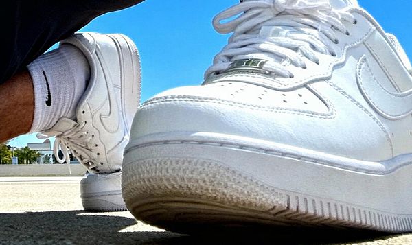 A close-up fisheye shot of white Nike Air Force 1 sneakers on a sunny day.
