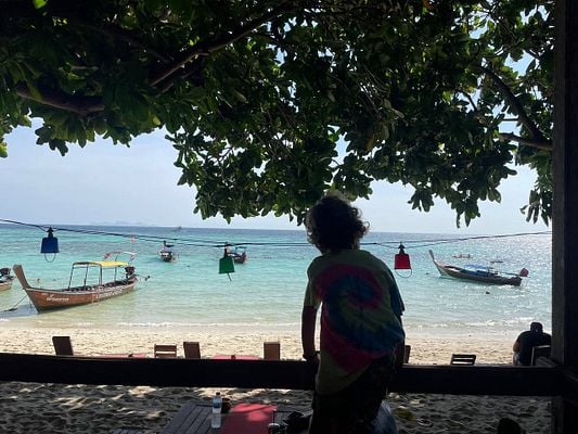 A serene beach scene featuring a person enjoying the view of boats on the water.