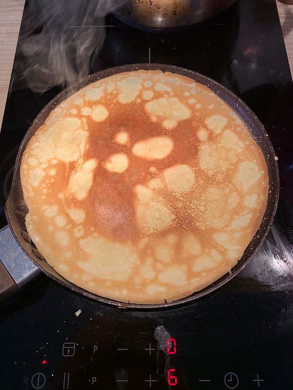 A crepe is being cooked in a frying pan on a stovetop.