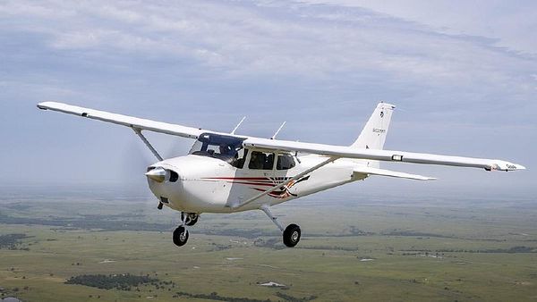 Side view photograph of a blue, white, and red Cessna 172 Skyhawk single-engine airplane on a grassy field.