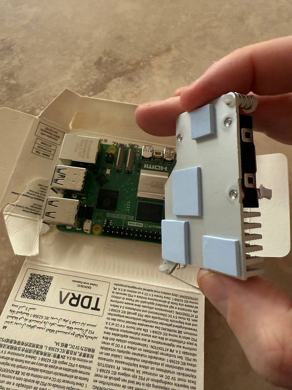 A person is holding a heatsink above a Raspberry Pi board inside its packaging.