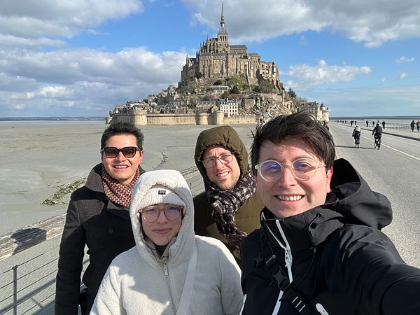 A group of four friends poses for a selfie in front of Mont Saint Michel.