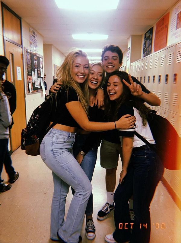 A group of four friends poses joyfully in a school hallway.