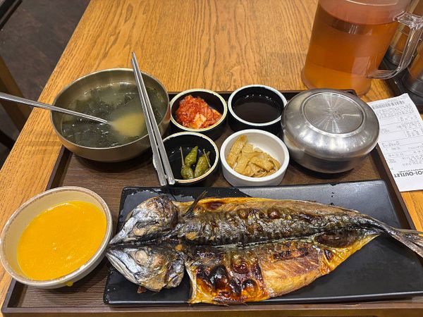 A Korean meal featuring grilled fish with various side dishes, soup, and rice on a wooden table.