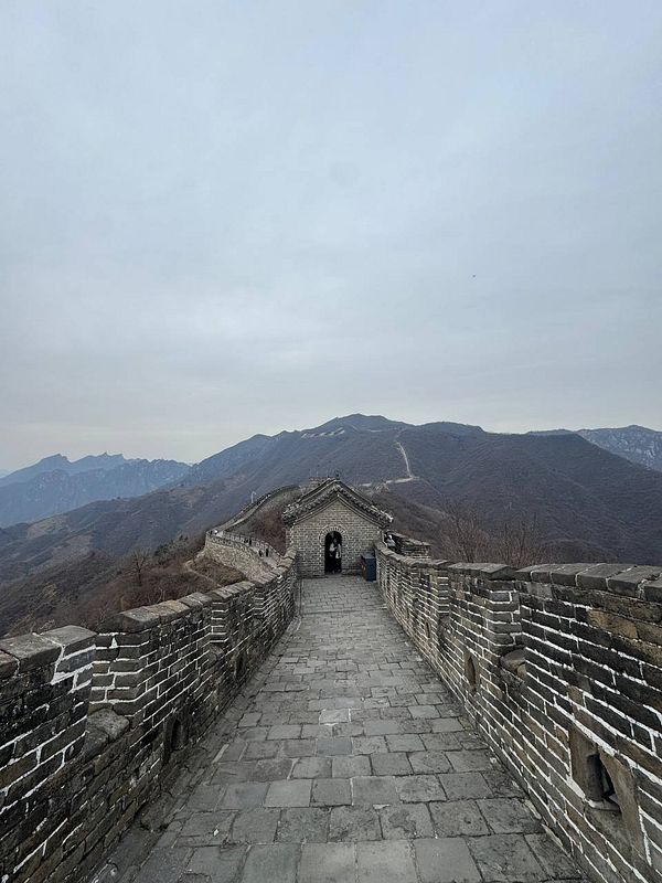 A scenic view of the Great Wall of China stretching towards the mountains under a cloudy sky.