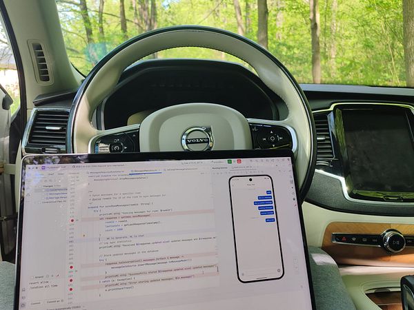 A person is working on a laptop inside a car parked in a wooded area.