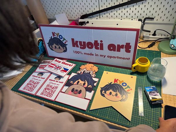 A workspace displaying a variety of colorful booth branding materials for 'kyoti art'.
