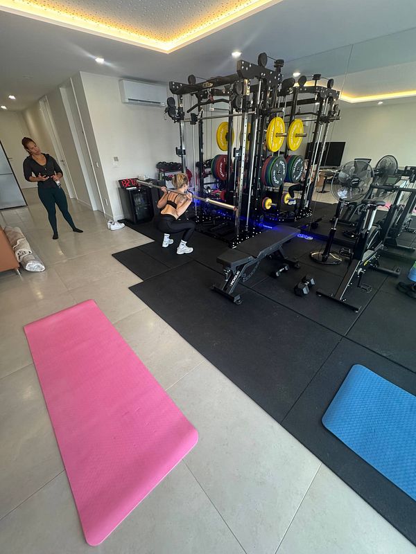 A personal training session is taking place in a well-equipped home gym.