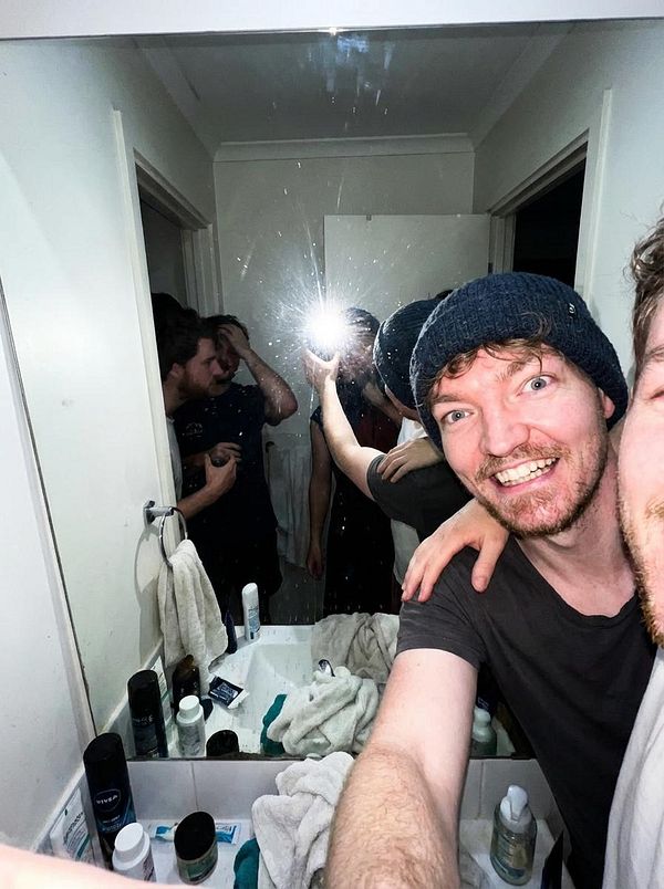 A group of friends takes a selfie in a bathroom with a mirror reflecting their playful moment.