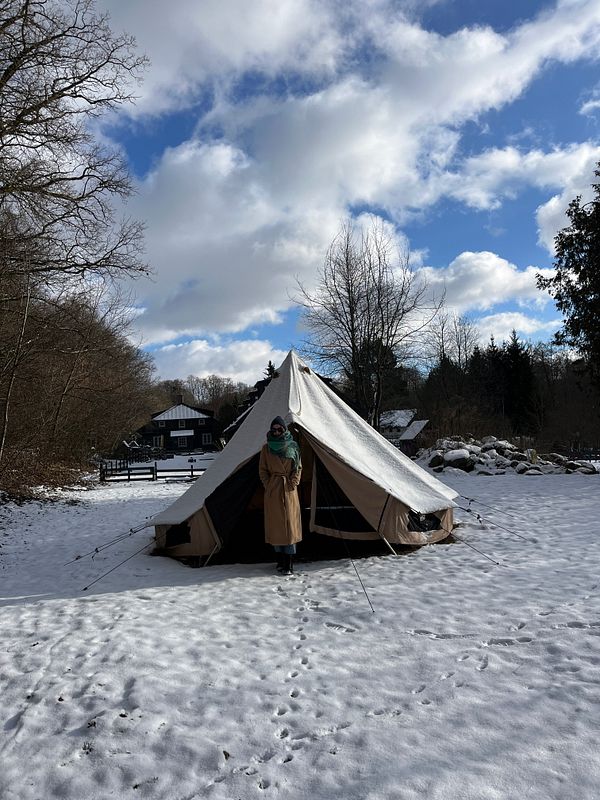 A person stands in front of a tent in a snowy landscape under a partly cloudy sky.