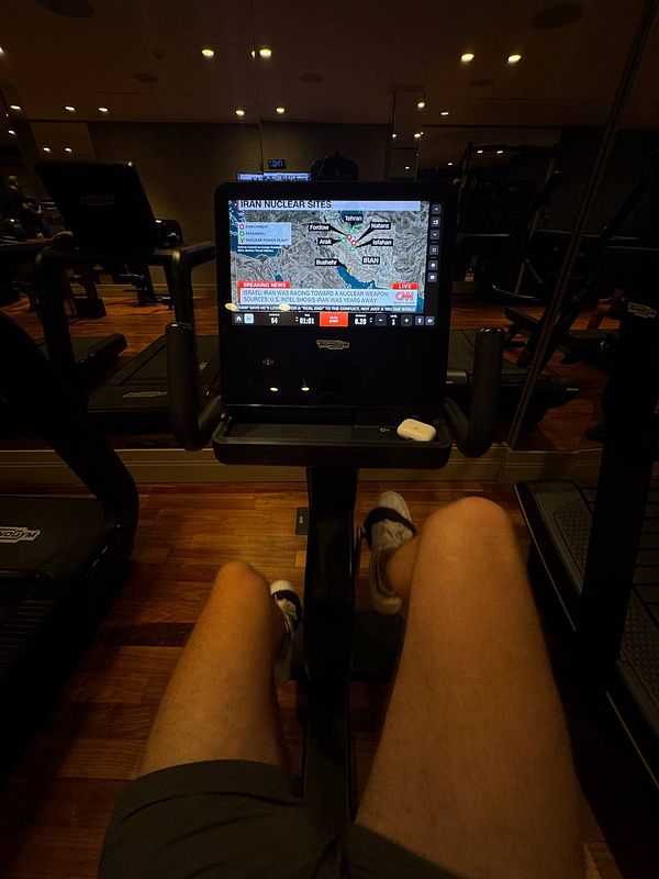 A person is exercising on a stationary bike in a hotel gym while watching a news broadcast.