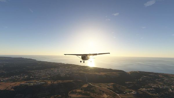 A small aircraft is flying over a coastal landscape during sunset.