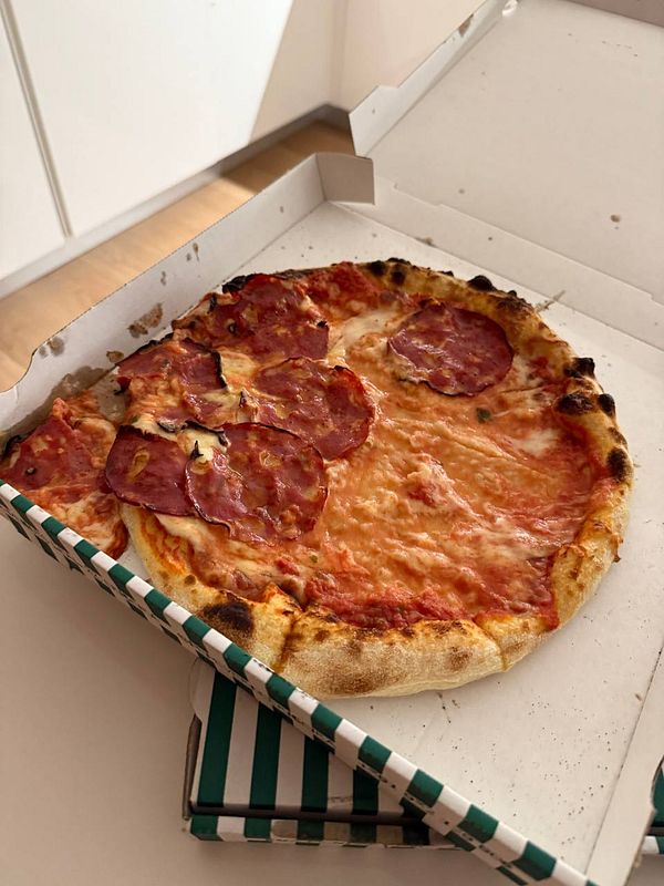 A pizza with slices of salami is presented in a takeout box.
