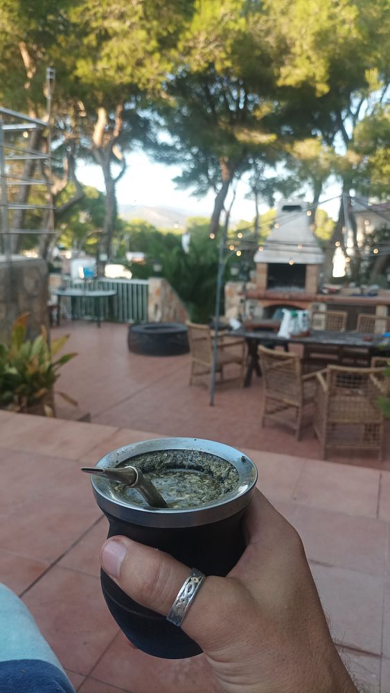 A hand holding a mate cup in a sunny terrace setting after cleaning up for a BBQ.