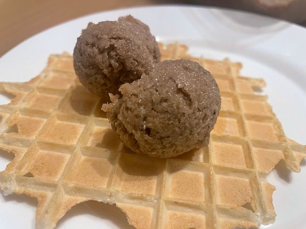 Two scoops of homemade banana ice cream placed on a square waffle on a white plate.