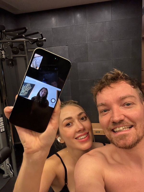 A man and a woman are taking a selfie in a gym while video calling a personal trainer.