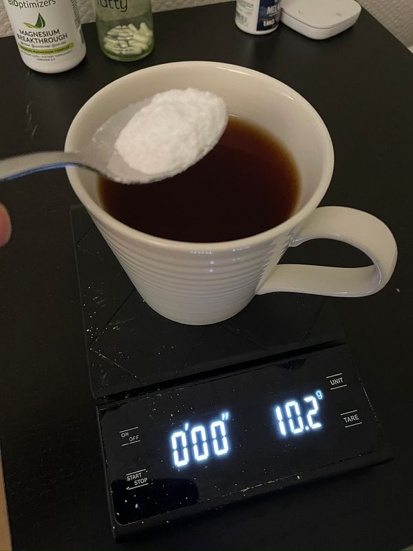 A spoonful of creatine is being added to a cup of English breakfast tea on a digital scale.