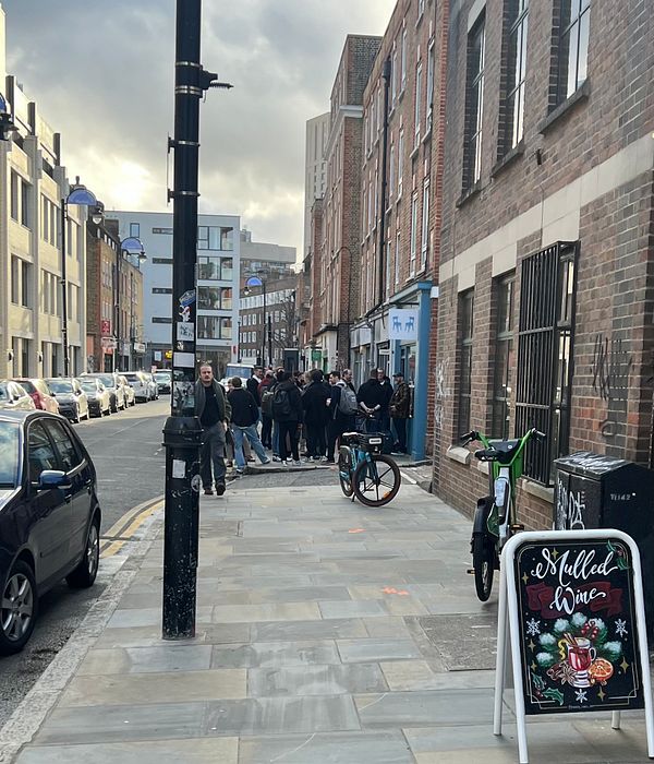 A bustling street scene with a crowd gathered outside a coffee shop, showcasing a mix of urban architecture and activity.