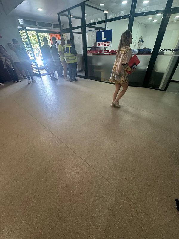 A busy driving test center with people waiting and a woman walking by.