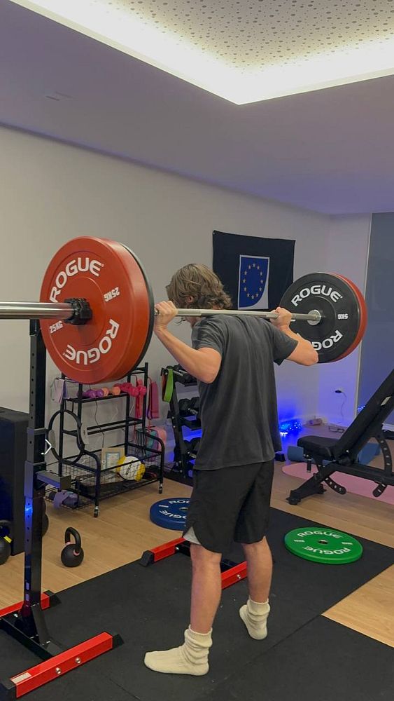 A person is performing a squat with a barbell in a home gym setting.