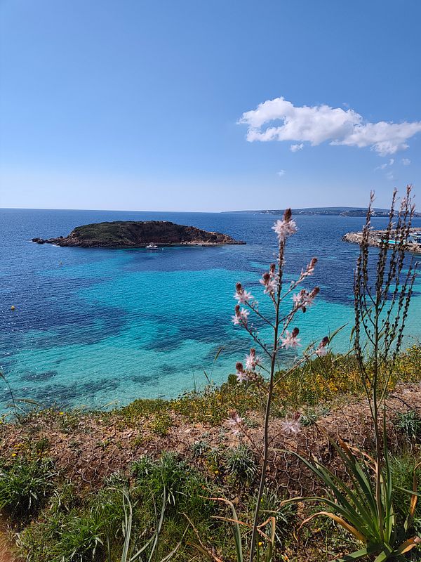 A couple hiking on a mountain ridge under a partly cloudy blue sky.