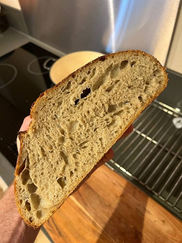 A slice of sourdough bread is being held up, showcasing its texture and crust.