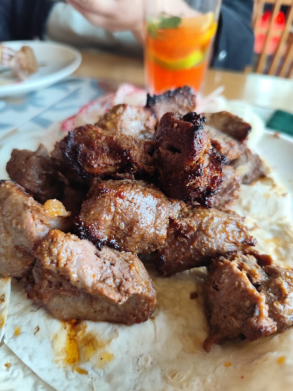 Grilled meat pieces served on flatbread with a glass of orange drink in the background.