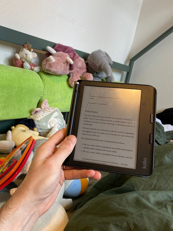 A person is reading AdonisJS documentation on a Kobo e-reader while surrounded by stuffed animals.