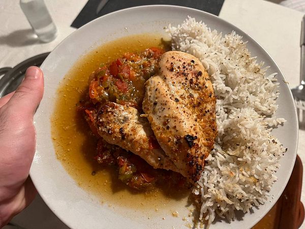 A plate of chicken with vegetables and rice is being held in a hand.