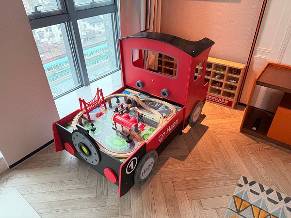 A cozy bedroom with a bed, wall shelves, a window with curtains, and various decorative items reflecting a personal, lived-in space.