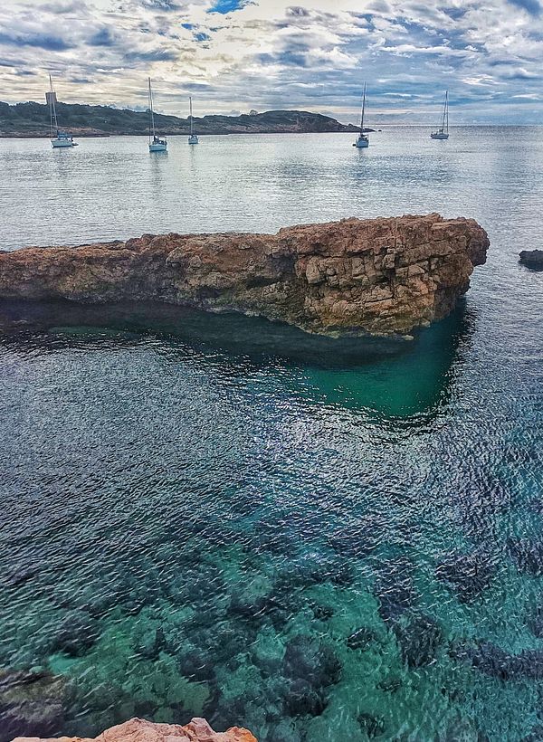A scenic coastal view featuring rocky formations and sailboats in calm waters.