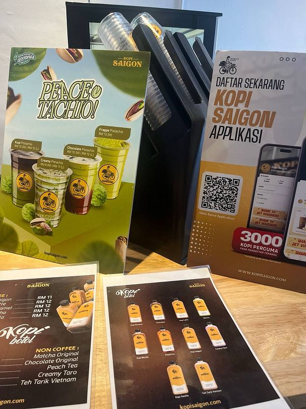 The image features a display of coffee and beverage options from Kopi Saigon, including promotional materials and menus.