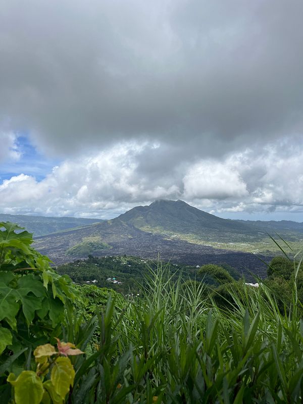 A scenic view of Mount Batur in Kintamani, surrounded by lush greenery and dramatic clouds.