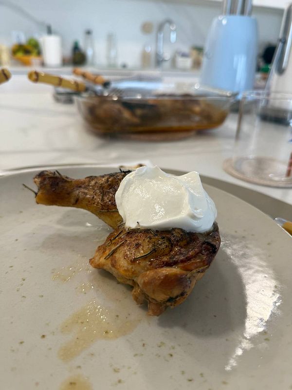 A piece of marinated chicken is served on a plate with a dollop of sour cream on top.